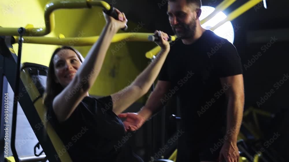 young woman and personal trainer flexing muscles on gym machine young woman and personal trainer flexing muscles on gym machine