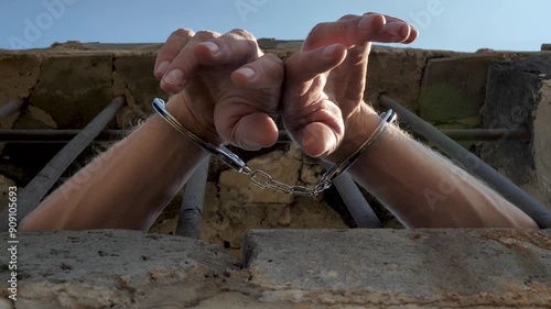 looking up male prisoner hands in metal handcuffs sticking out of prison window. Man handcuffed to bars. Prisoner's hands hanging out of cage. Concept of fighting organized crime photo