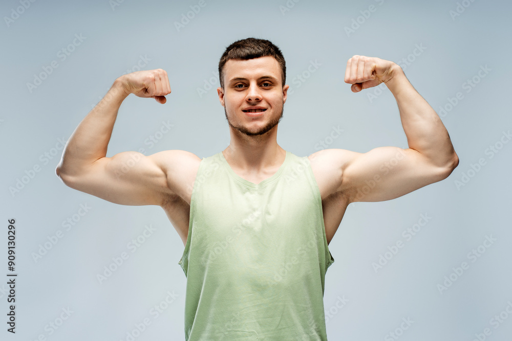 Naklejka premium Athletic man flexing muscles showing biceps triceps on grey background looking at camera