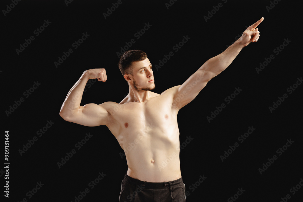 Strong athletic man flexing muscles and pointing upwards isolated on black background Strong athletic man flexing muscles and pointing upwards isolated on black background