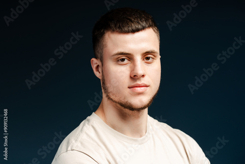 Young, smiling man with short hair posing on dark blue background, looking at camera