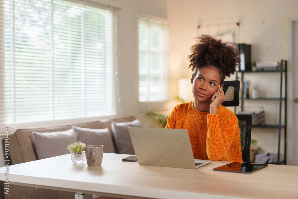 Young black woman in cozy sweater concentrating on laptop at home office during daytime. Young black woman in cozy sweater concentrating on laptop at home office during daytime.