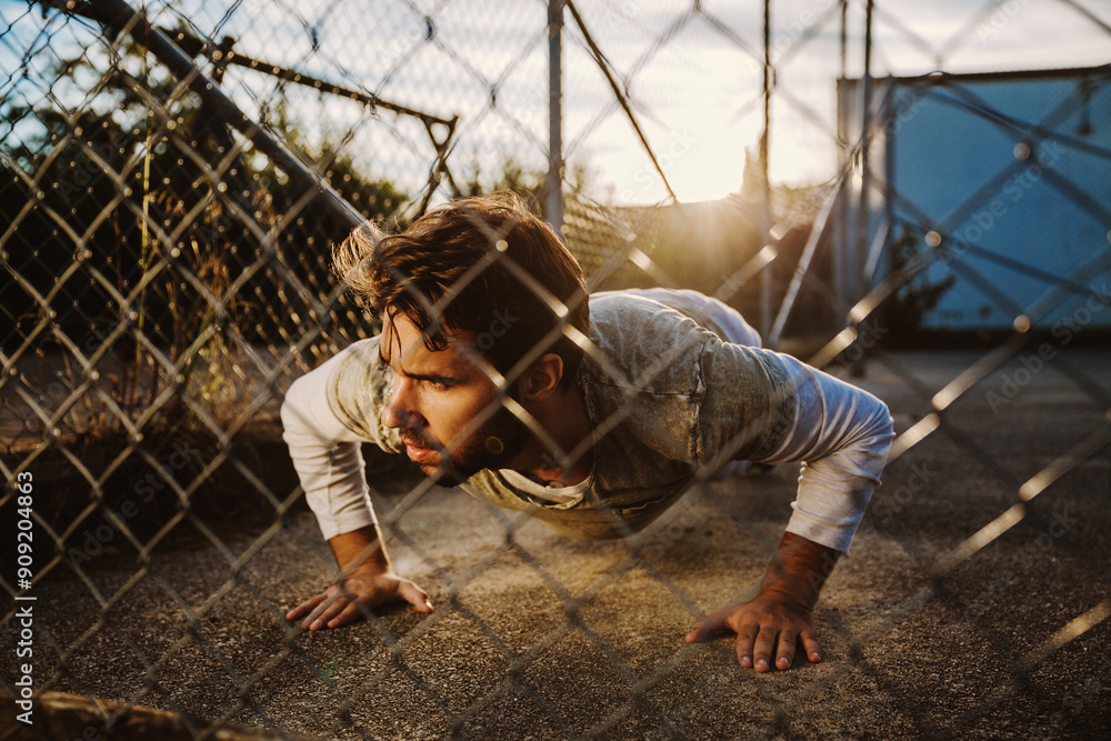 Man doing push-ups outside in fenced area during sunset workout Man doing push-ups outside in fenced area during sunset workout