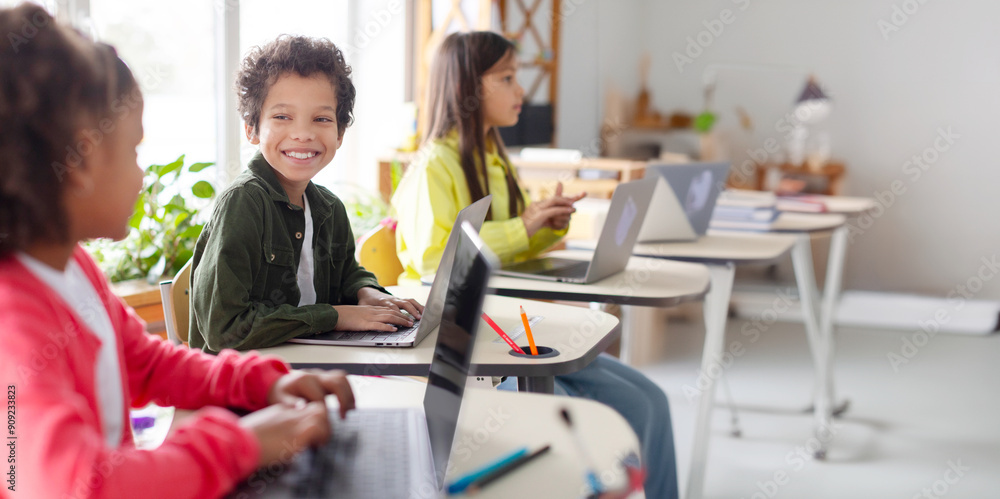 Group of children sitting in school classroom with laptops on desk, talking with each other, studying. Classmates study in classroom. Back to school. Group of children sitting in school classroom with laptops on desk, talking with each other, studying. Classmates study in classroom. Back to school.