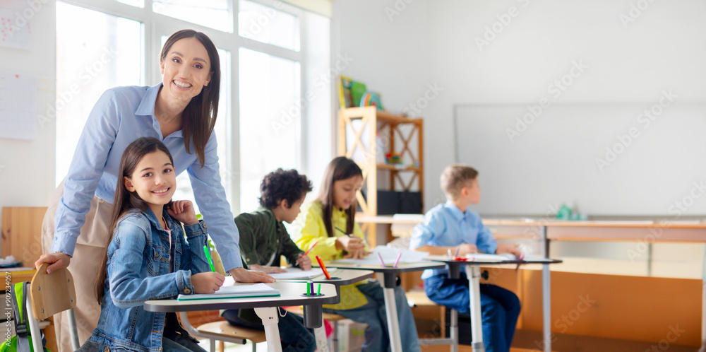 Cheerful young female teacher working in elementary school, happy teacher and girl smiling at camera in classroom interior Cheerful young female teacher working in elementary school, happy teacher and girl smiling at camera in classroom interior