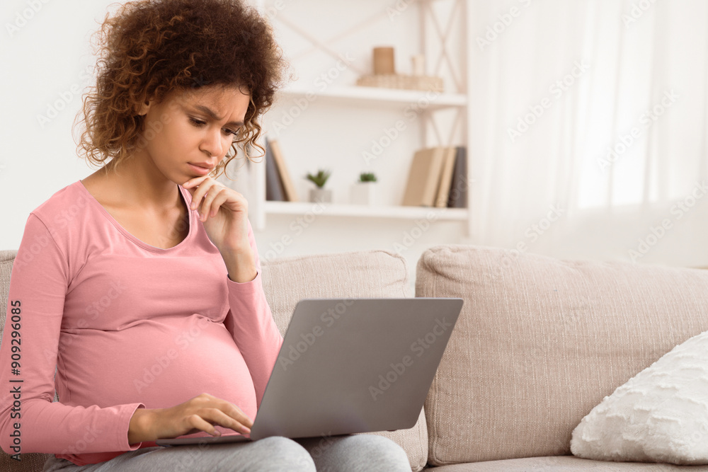 Confused afro expectant woman using laptop, buying goods for newborn baby, free space Confused afro expectant woman using laptop, buying goods for newborn baby, free space