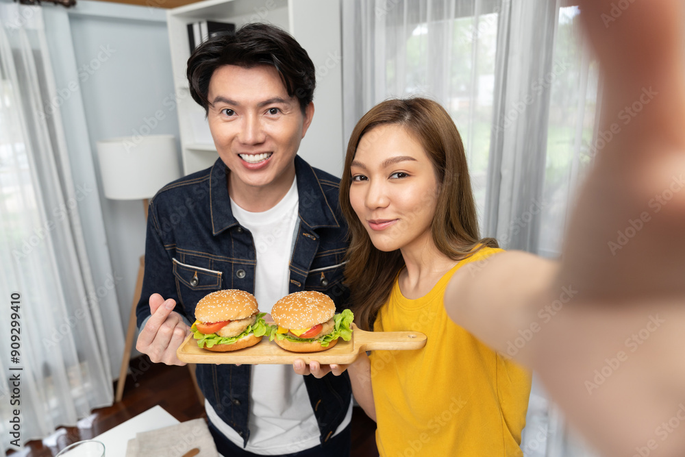 Smiling host chef influencers taking photo with smartphone by selfie straight view holding double hamburger on cooking show special easy dish homemade on social media channel live streaming. Infobahn. Smiling host chef influencers taking photo with smartphone by selfie straight view holding double hamburger on cooking show special easy dish homemade on social media channel live streaming. Infobahn.
