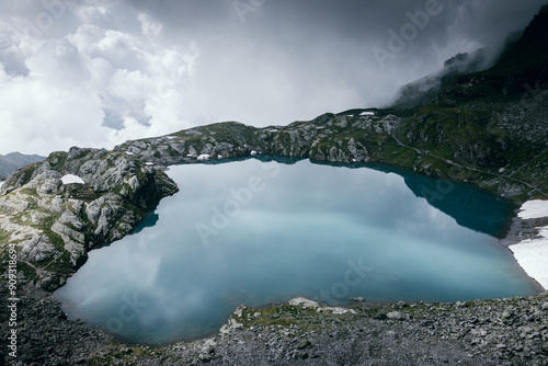 Der Himmel reisst auf über türkisblauem Bergsee fast in Herzform photo