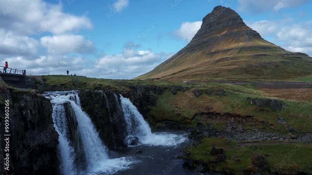 Iconic Kirkjufell mountain with its symmetrical shape and Kirkjufellsfoss waterfall cascading into a serene pool, bathed in warm sunlight under a partly cloudy sky. Iconic Kirkjufell mountain with its symmetrical shape and Kirkjufellsfoss waterfall cascading into a serene pool, bathed in warm sunlight under a partly cloudy sky.