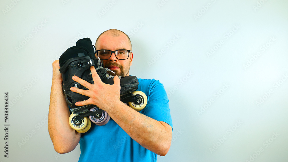 Portrait of handsome bearded man skater in blue shirt with glasses hugging his rollerblades, isolated on white background, extreme sport gear