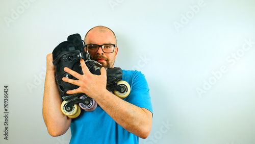 Portrait of handsome bearded man skater in blue shirt with  glasses hugging his rollerblades, isolated on white background, extreme sport gear