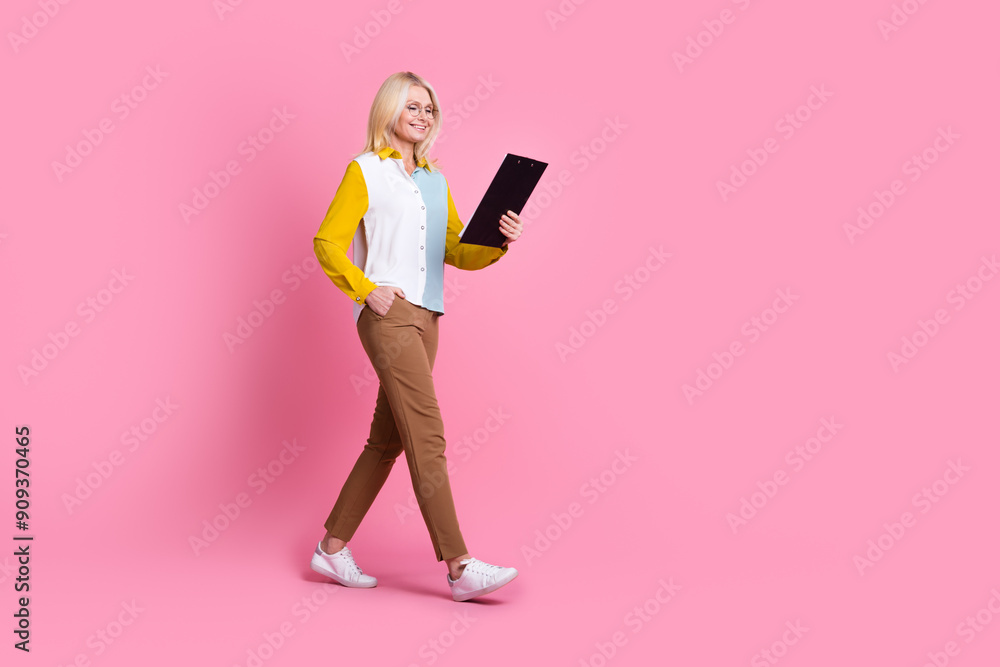 Full size photo of nice aged lady walk read clipboard empty space wear shirt isolated on pink color background Full size photo of nice aged lady walk read clipboard empty space wear shirt isolated on pink color background