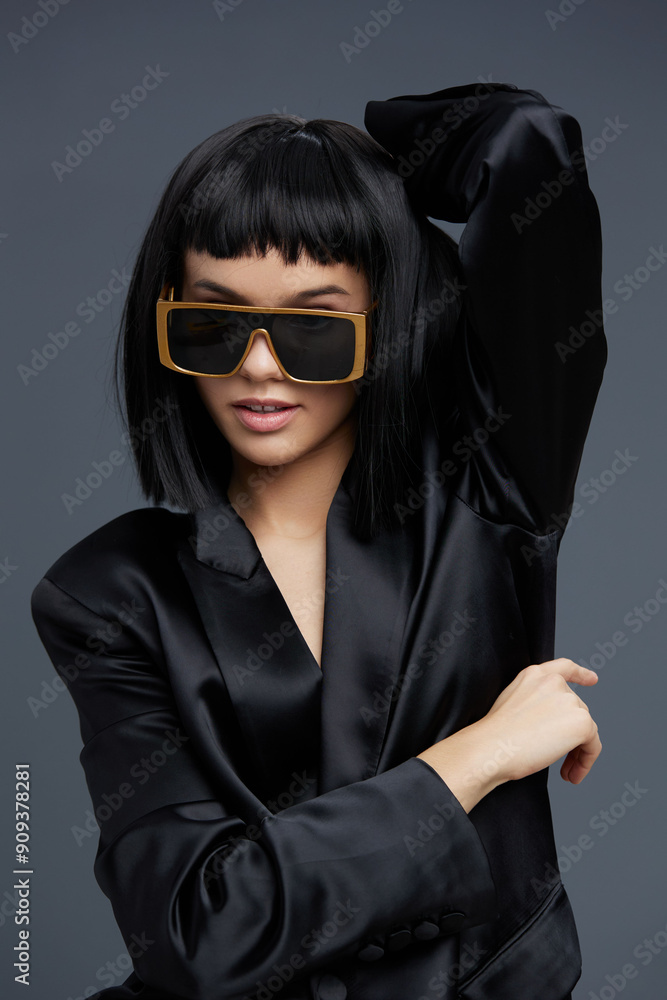 Woman in black suit and sunglasses, posing confidently with hands on hips and head tilted to the side, exuding sophistication and style against a neutral background Woman in black suit and sunglasses, posing confidently with hands on hips and head tilted to the side, exuding sophistication and style against a neutral background