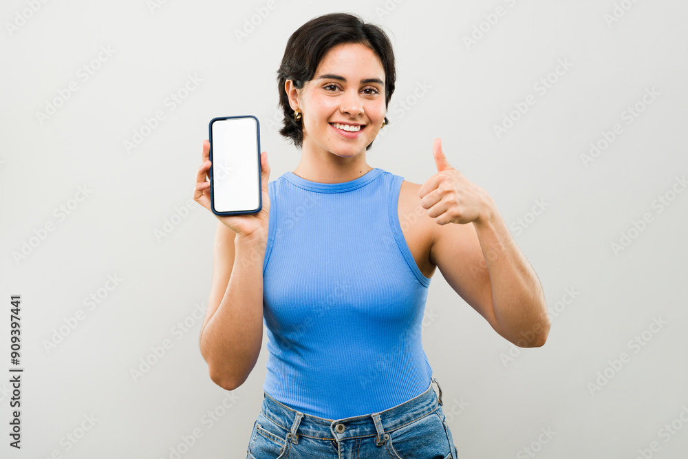 Smiling young woman holding smartphone with blank screen and giving thumbs up gesture Smiling young woman holding smartphone with blank screen and giving thumbs up gesture