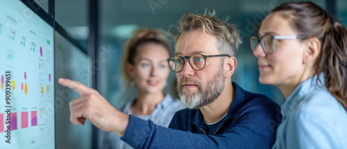A team of three professionals, including a senior man with glasses and a beard, collaborating on data analysis using a large screen in a modern office.
