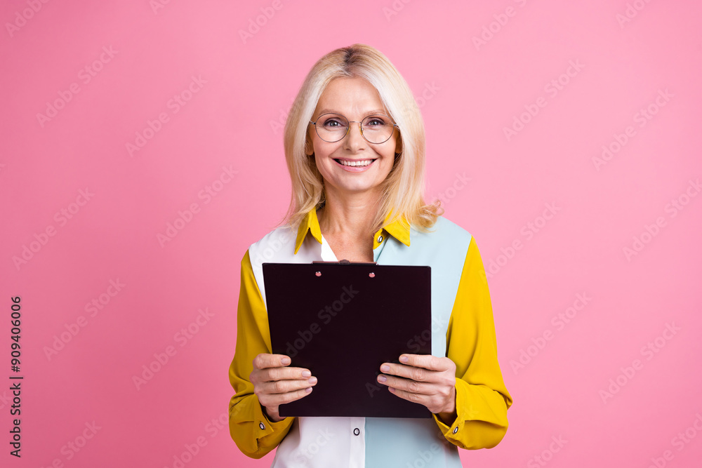 Photo of nice aged lady hold clipboard wear shirt isolated on pink color background Photo of nice aged lady hold clipboard wear shirt isolated on pink color background