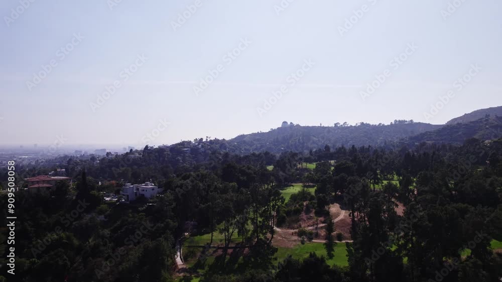 A serene aerial view capturing the lush greenery of Los Angeles hills with the iconic Griffith Observatory visible in the distance. The clip highlights the natural beauty and tranquility of the area. A serene aerial view capturing the lush greenery of Los Angeles hills with the iconic Griffith Observatory visible in the distance. The clip highlights the natural beauty and tranquility of the area.