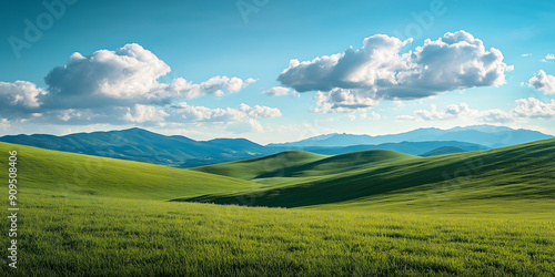 Landscape portrait of emerald green rolling hills with a forest off in the distance, blue sky and white puffyy clouds in the background over mountains