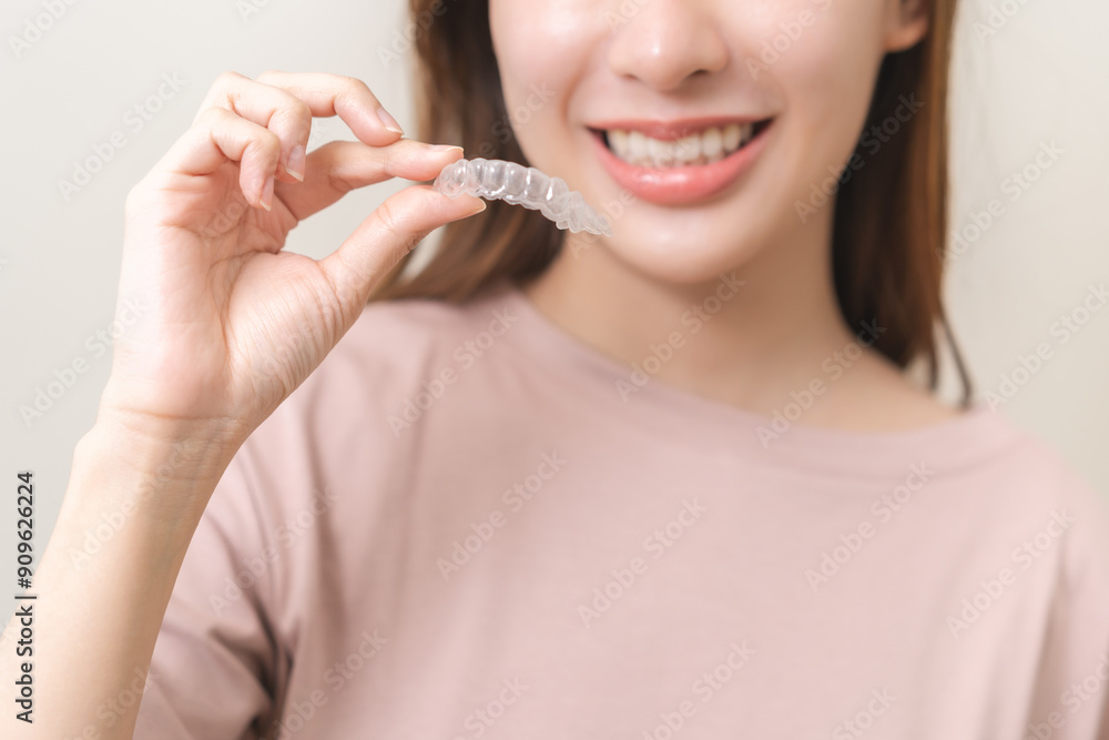 Dental invisible braces, beautiful smiling asian young woman holding invisalign braces, wearing orthodontic silicone trainer, white smile using invisible whitening tray. Stomatology, dental healthcare Dental invisible braces, beautiful smiling asian young woman holding invisalign braces, wearing orthodontic silicone trainer, white smile using invisible whitening tray. Stomatology, dental healthcare