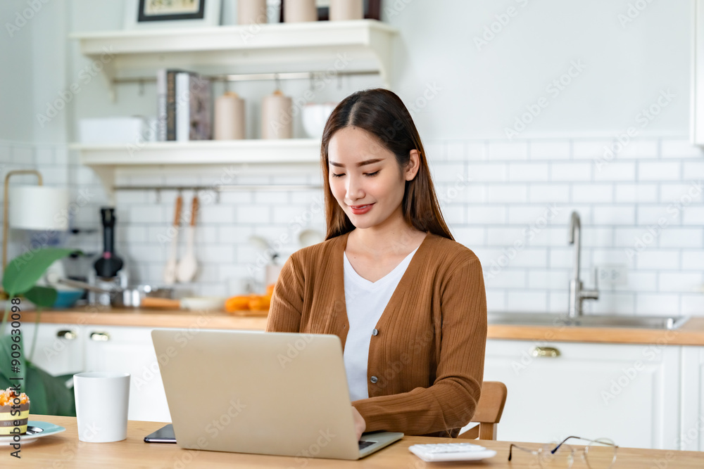 Beautiful young Asian woman working with laptop computer in home kitchen. Work at home Beautiful young Asian woman working with laptop computer in home kitchen. Work at home