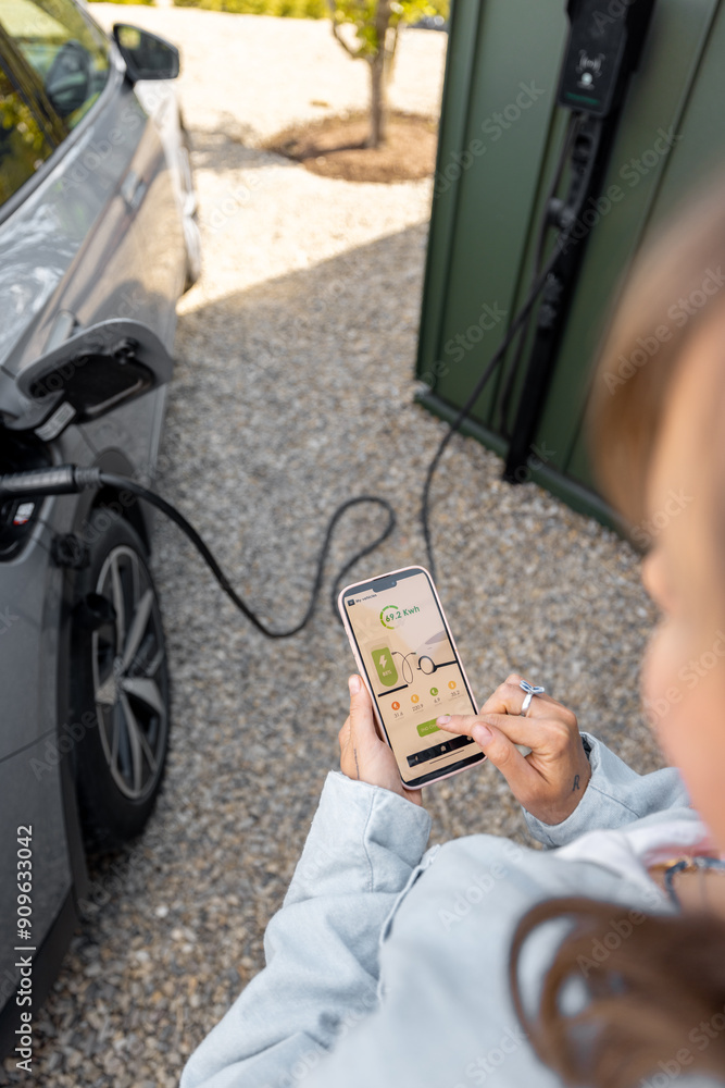 Woman using smartphone with launched application for car charging, controlling the charging process remotely. Smart technologies and app design concept Woman using smartphone with launched application for car charging, controlling the charging process remotely. Smart technologies and app design concept