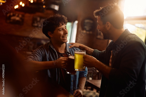 Happy man and his friend toasting while drinking beer in bar.