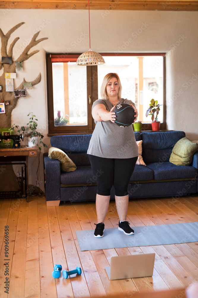 Φωτογραφία Online fitness training for overweight woman exercising at home, using weighted medicine ball