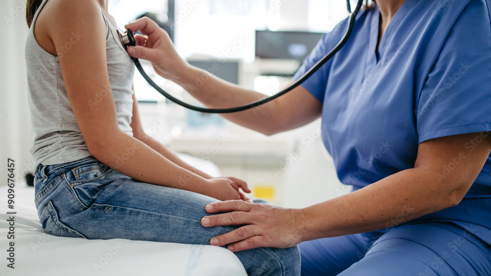 Obraz premium Doctor examining young girl, listening to heartbeat, breathing, using stethoscope. School entry medical exam.
