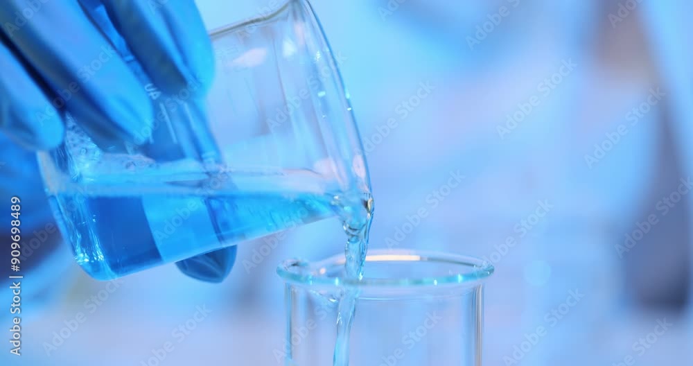 Scientist laboratory assistant pours blue liquid from glass beaker into a test tube in the laboratory Scientist laboratory assistant pours blue liquid from glass beaker into a test tube in the laboratory