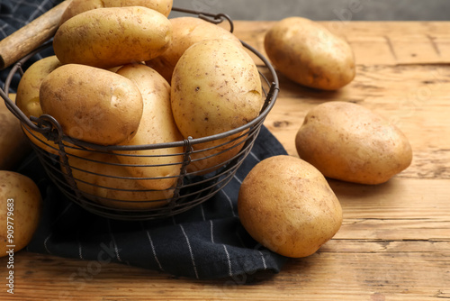 Many fresh potatoes in metal basket on wooden table, closeup photo