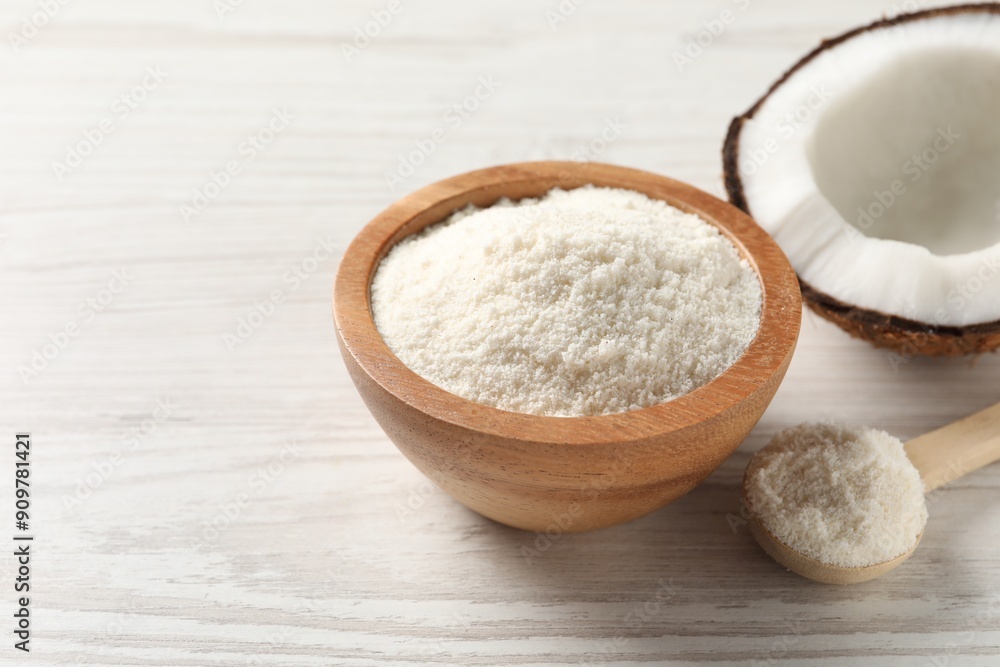 Fresh coconut flour in bowl, spoon and nut on white wooden table, space for text Fresh coconut flour in bowl, spoon and nut on white wooden table, space for text