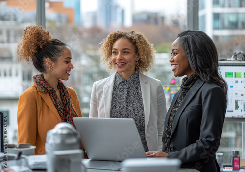 Obraz na płótnie Portrait of three smiling colleagues, dark skin women standing together at table with laptop and talking during meeting in office on background of city downtown w salonie