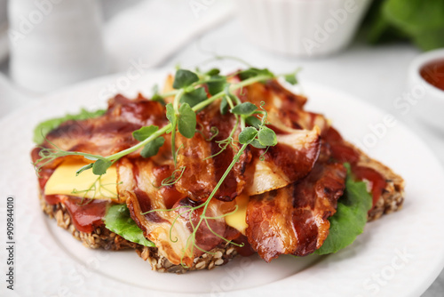 Tasty sandwich with bacon and microgreens on white table, closeup