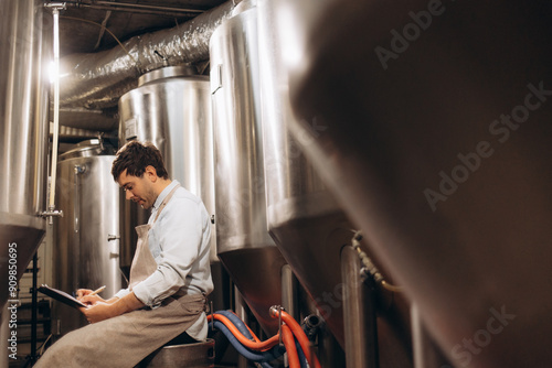 Man working in craft brewery examining production of the beer.