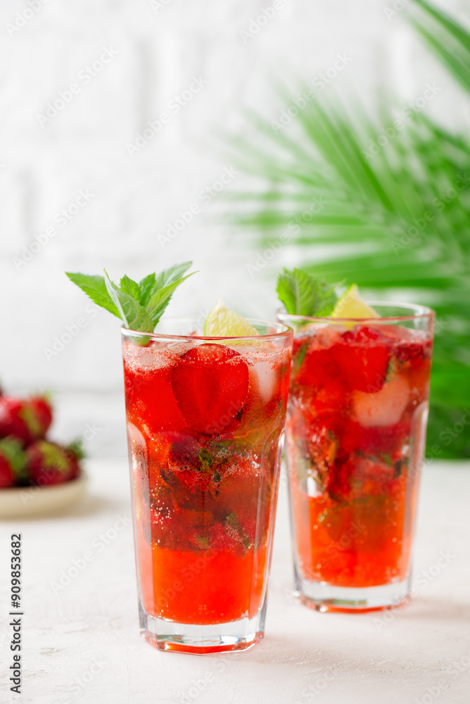 Mojito cocktail with strawberries, lime and mint on a background of a palm branch. Strawberry Mojito. Sugar free, nonalcoholic. Vertical orientation. Mojito cocktail with strawberries, lime and mint on a background of a palm branch. Strawberry Mojito. Sugar free, nonalcoholic. Vertical orientation.