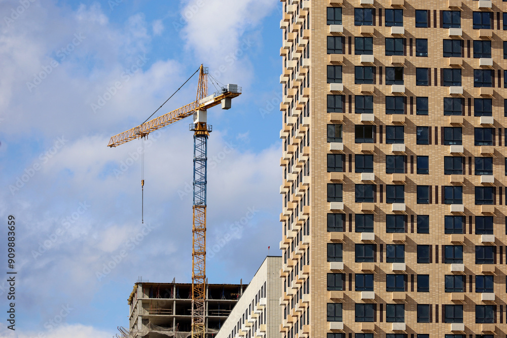 Tower crane and unfinished buildings on background of blue sky. Housing construction, apartment blocks in city Tower crane and unfinished buildings on background of blue sky. Housing construction, apartment blocks in city