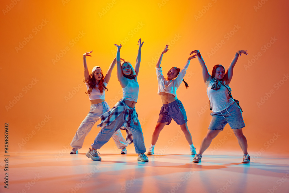 Αυτοκόλλητο Dancers in casual outfits dance contemp synch against bright orange backdrop, shows unique styles and vibrant dance moves