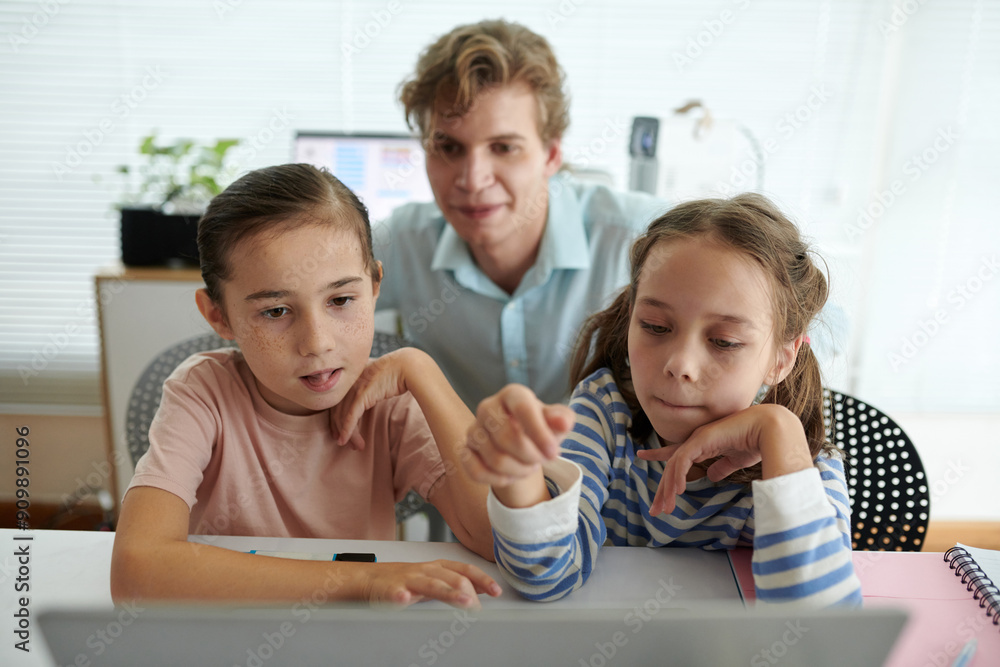 Children focusing on technology with guidance from adult in educational setting creating interactive learning experience Children focusing on technology with guidance from adult in educational setting creating interactive learning experience
