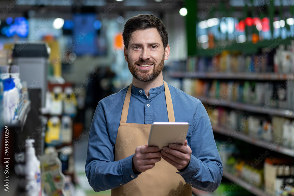 Smiling supermarket worker using digital tablet for inventory management in store aisle. Employee wearing apron holding tablet, performing inventory management tasks. Modern retail technology Smiling supermarket worker using digital tablet for inventory management in store aisle. Employee wearing apron holding tablet, performing inventory management tasks. Modern retail technology
