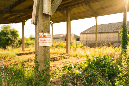 Shallow focus of a sign warning of a Fragile Roof seen in an empty barn in rural England. Members of the public have previously fallen from the fragile barn roof which is made of asbestos.