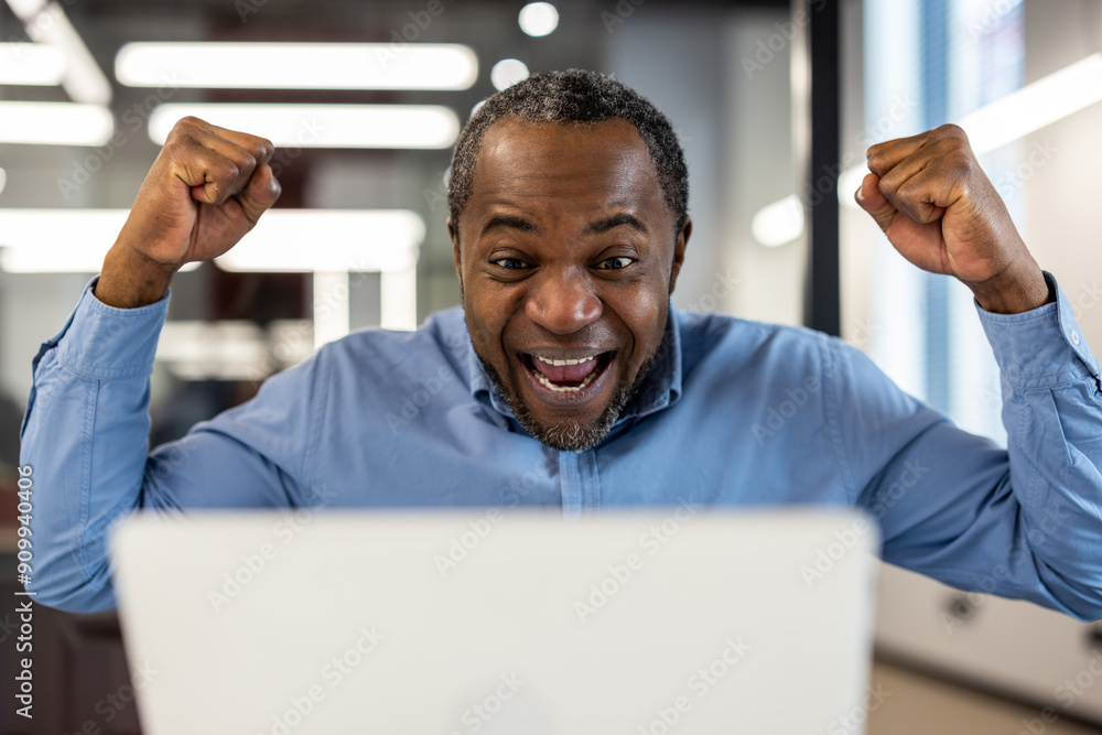 Happy businessman celebrating success at work on laptop. Man with raised fists showing joy and excitement while looking at screen. Concept of achievement, victory, and career success. Happy businessman celebrating success at work on laptop. Man with raised fists showing joy and excitement while looking at screen. Concept of achievement, victory, and career success.