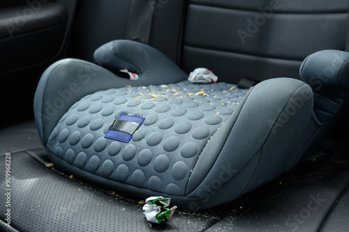 Child car seat, booster, securely fastened to back seat of car, providing comfort and safety for small passengers. Child car seat in crumbs and candy wrappers after child trip in the car