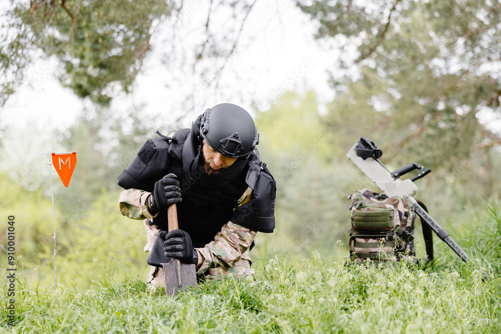 A man in a military uniform and a bulletproof vest works in the forest to demine the territory. A man warns of danger by making a red mark A man in a military uniform and a bulletproof vest works in the forest to demine the territory. A man warns of danger by making a red mark