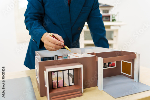 Asian architect in a formal suit works alone at his desk with a laptop, paperwork, tablet, and calculator, drawing blueprints for a home and land mortgage project. photo