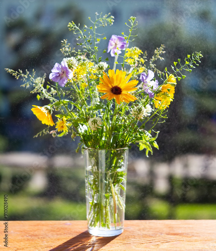 Bouquet of wild flowers in a glass vase on a wooden window sill.