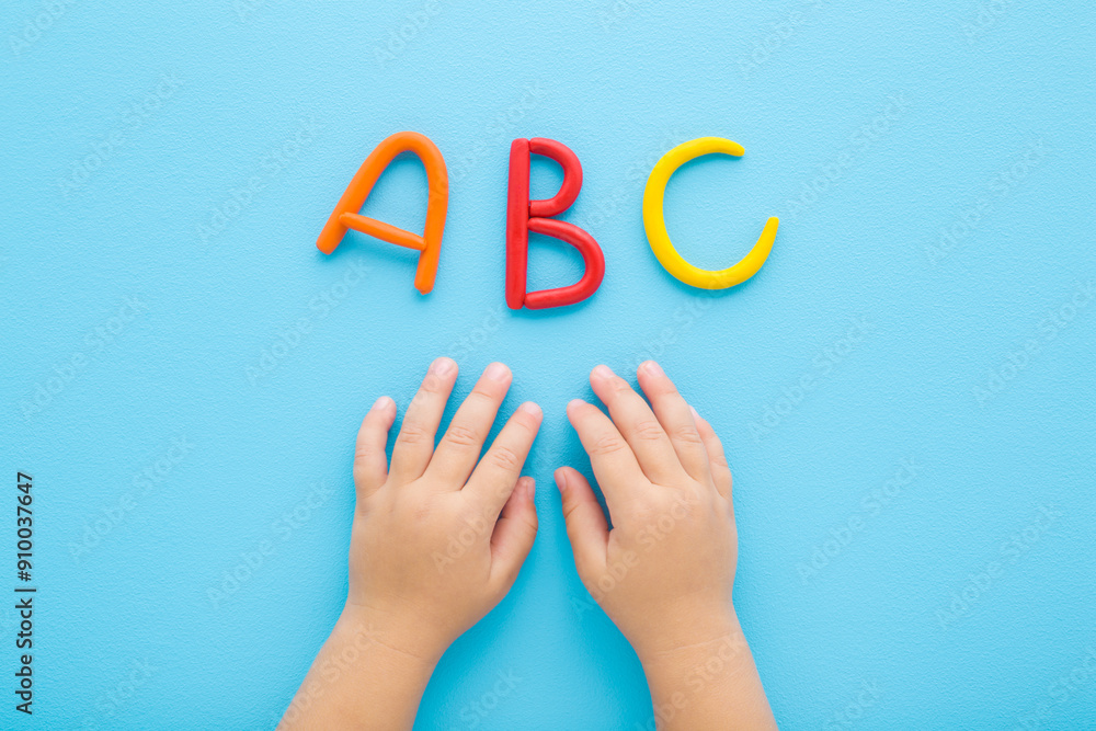 Baby boy hands and colorful abc letters created from modeling clay on light blue table background. Pastel color. Time to learning. Closeup. Point of view shot. Top down view. Baby boy hands and colorful abc letters created from modeling clay on light blue table background. Pastel color. Time to learning. Closeup. Point of view shot. Top down view.