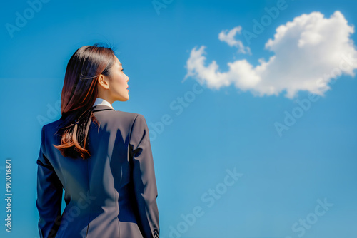 Back view of businesswoman in a suit looking up at a clear blue sky.