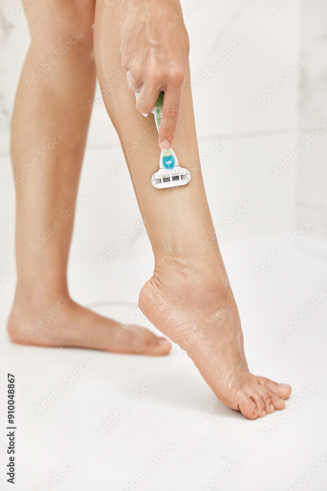 Fototapeta premium Young woman shaving her legs with razor in white shower, close-up