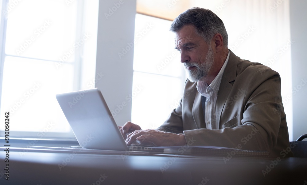 Smiling mature business man executive wearing shirt sitting at desk using laptop. Happy busy professional middle aged businessman investor working on computer looking away in office Smiling mature business man executive wearing shirt sitting at desk using laptop. Happy busy professional middle aged businessman investor working on computer looking away in office