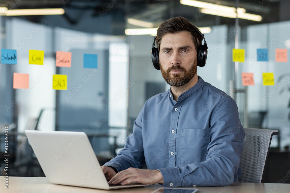 Focused professional working on laptop in modern office with headphones Focused professional working on laptop in modern office with headphones